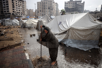 Una mujer trata de achicar el agua que inunda las tiendas de desplazados en Ciudad de Gaza.