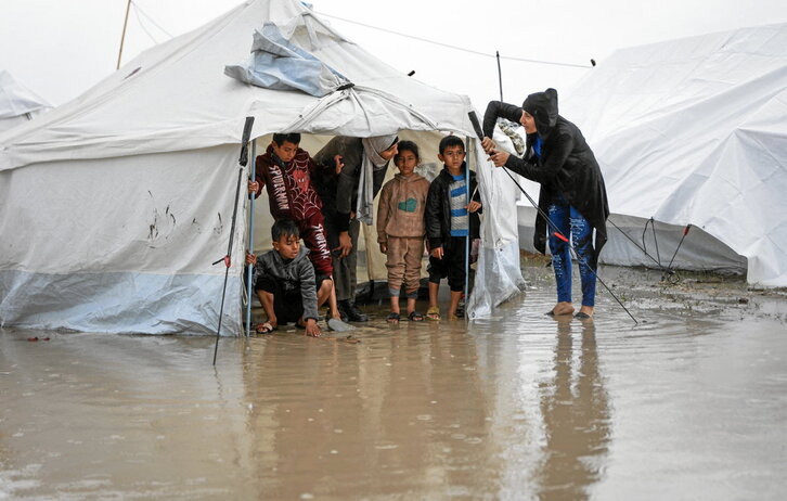 Niños en chancletas se cubren en una tienda del temporal de frío y lluvía que ha convertido el suelo en un lodazal.