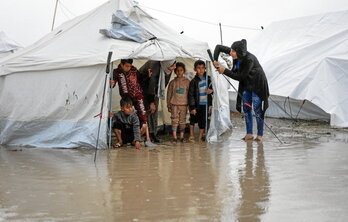 Niños en chancletas se cubren en una tienda del temporal de frío y lluvía que ha convertido el suelo en un lodazal.