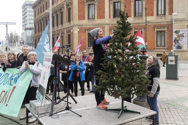 Una trabajadora de Benito Menni cuelga una de las reivindicaciones de la plantilla en el pino navideño instalado ante el Parlamento navarro.