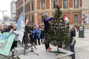 Una trabajadora de Benito Menni cuelga una de las reivindicaciones de la plantilla en el pino navideño instalado ante el Parlamento navarro.