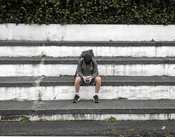 Un joven adolescente de Azkaine sentado en unos escalones él solo mientras pone toda su atención en el móvil que se encuentra entre sus manos.