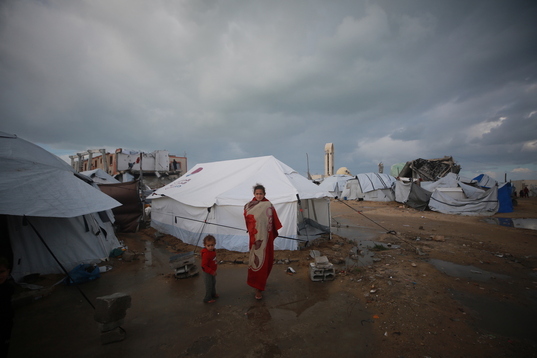 Palestinos desplazados junto a un gran charco de agua y barro en un campamento de tiendas junto a la costa, en la ciudad de Gaza.