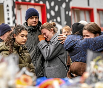 Varios jóvenes lloran cerca del bar incendiado.