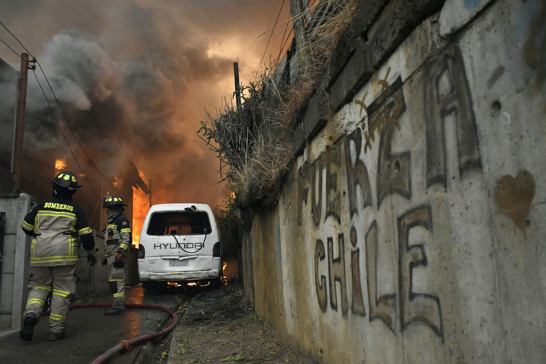 Bomberos intentan extinguir una casa en llamas durante un incendio forestal en Concepción.