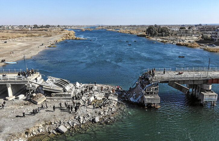 Un grupo de personas intenta cruzar las ruinas de un puente destruido a orillas del Éufrates en la ciudad de Raqqa.