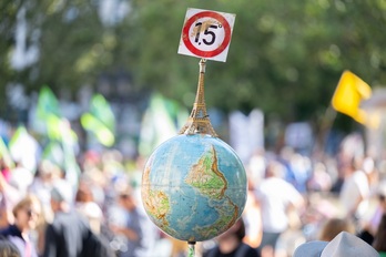 Un hombre lleva un globo terráqueo con una Torre Eiffel en miniatura y el objetivo de 1,5 grados del Acuerdo de París durante una manifestación en Frankfurt.