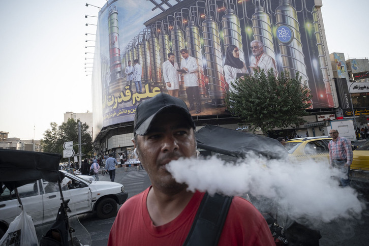Un viandante camina por Teherán con  imágenes simbólicas de la instalación nuclear de Natanz al fondo.