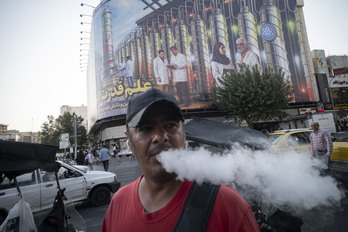 Un viandante camina por Teherán con  imágenes simbólicas de la instalación nuclear de Natanz al fondo.