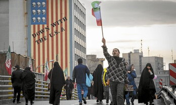 Un hombre enarbola la bandera iraní frente a un mural contra Estados Unidos en Teherán.