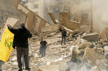 Un partidario de Hizbulah ondea una bandera de la organización sobre unas ruinas en Beirut.