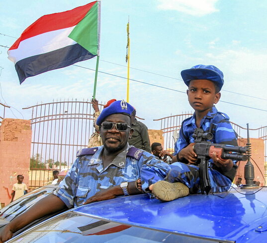 Un niño sostiene una pistola de plástico junto a un policía sudanés, durante un desfile en Jartum el 23 de agosto de 2025.