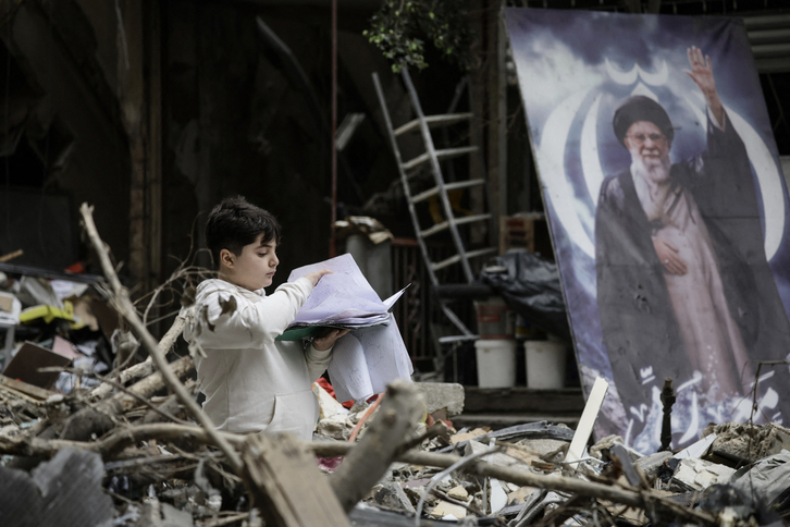 Un niño entre los escombros de un edificio destruido, junto a un retrato del anterior líder supremo iraní, el ayatollah Ali Jamenei