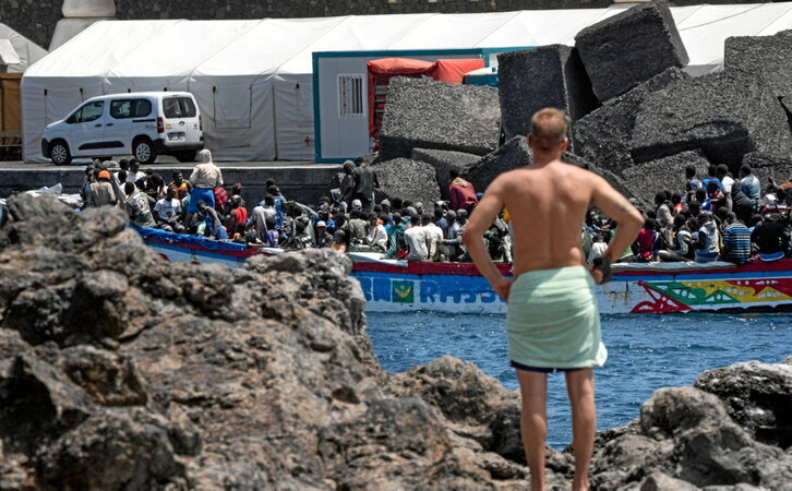Un bañista observa cómo un cayuco llega al puerto de La Restinga, en la isla canaria de El Hierro.