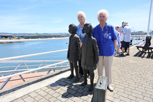 Dos de aquellas ‘niñas de la guerra’, este sábado en Santurtzi junto a las estatuas que rememoran aquella triste marcha.
