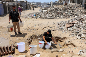 Un hombre llena cubos de agua de los restos de tuberías en uno de los barrios devastados de Ciudad de Gaza.