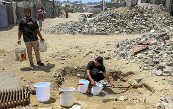 Un hombre llena cubos de agua de los restos de tuberías en uno de los barrios devastados de Ciudad de Gaza.