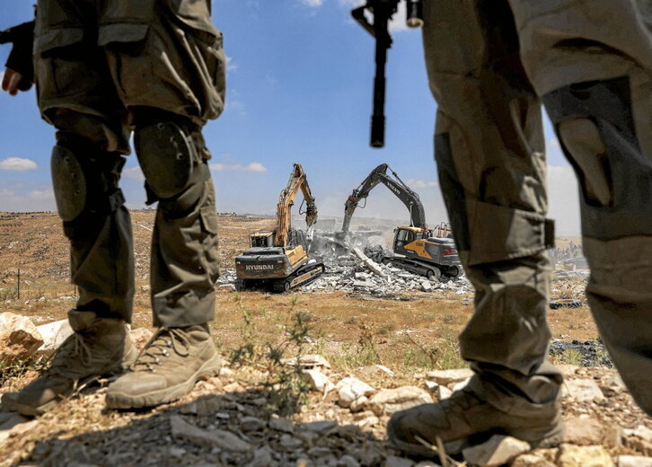 Fuerzas israelíes hacen guardia mientras demuelen una vivienda palestina.