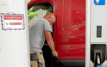 Trabajador repostando en una gasolinera de Roma. Los precios del diésel en Italia están en máximos históricos. A la izquierda, pantalla con los precios en Bruselas, de récord también.