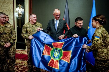El canciller alemán, Friedrich Merz, y el presidente ucraniano, Volodimir Zelensky, entregan una bandera firmada a soldados ucranianos.