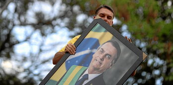 Flávio Bolsonaro alzando un retrato de su padre y expresidente de Brasil, Jair Bolsonaro durante un mitin.