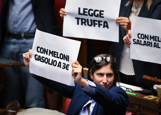 La secretaria del PD, Elly Schlein, y miembros de su partido sostienen carteles contra la nueva ley electoral y la subida de precios en el debate del jueves.