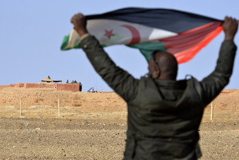 Un saharaui muestra su bandera a los soldados marroquíes del muro levantado en el Sahara Occidental ocupado.