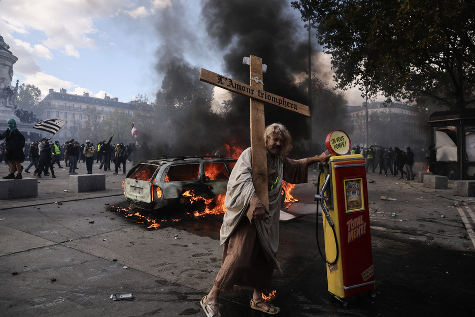Un manifestante sostiene una cruz con una inscripción que dice «el amor triunfará» junto a un surtidor de gasolina. Un manifestante sostiene una cruz con una inscripción que dice «el amor triunfará» junto a un surtidor de gasolina.