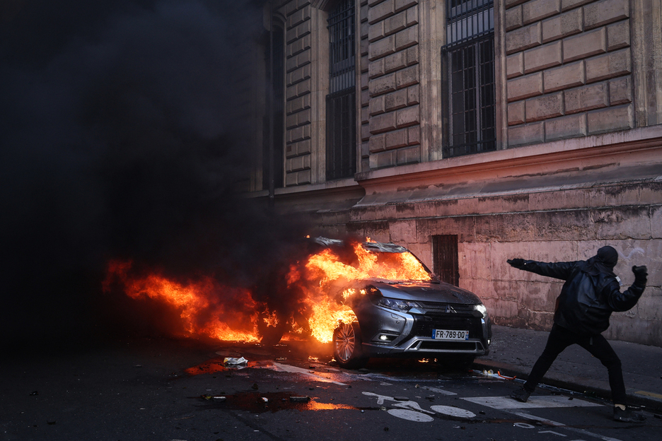 Un manifestante lanza un proyectil frente a un automóvil en llamas. Un manifestante lanza un proyectil frente a un automóvil en llamas.