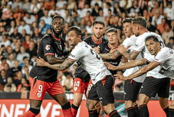 Jugadores de los dos equipos aguardan el balón en el área.